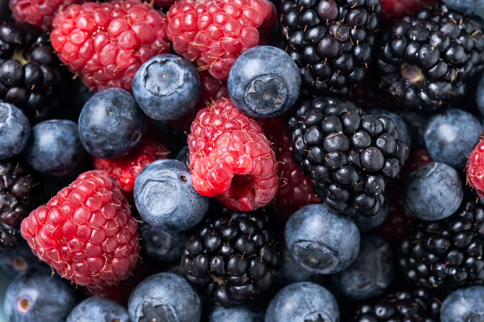 A vibrant close-up of a mix of ripe blueberries, red raspberries, and dark blackberries, showcasing a sweet and natural summer food source for deer
